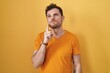 © Krakenimages.com - Young hispanic man standing over yellow background thinking concentrated about doubt with finger on chin and looking up wondering