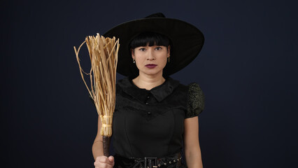 Sticker - Young chinese woman wearing witch costume holding broom over isolated black background