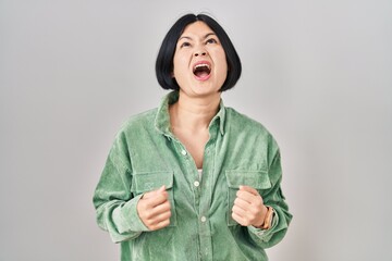 Poster - Young asian woman standing over white background angry and mad screaming frustrated and furious, shouting with anger. rage and aggressive concept.