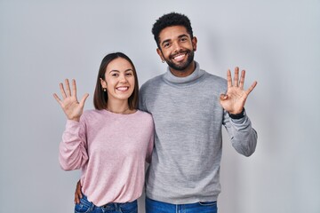 Sticker - Young hispanic couple standing together showing and pointing up with fingers number nine while smiling confident and happy.