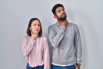 Wall Mural - Young hispanic couple standing together touching painful neck, sore throat for flu, clod and infection