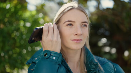 Poster - Young blonde woman listening to voice message at park