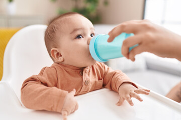 Poster - Adorable hispanic toddler drinking water sitting on highchair at home