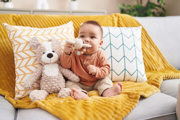 Sticker - Adorable hispanic toddler bitting toy sitting on sofa at home