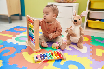 Sticker - Adorable hispanic toddler playing with abacus sitting on floor at kindergarten