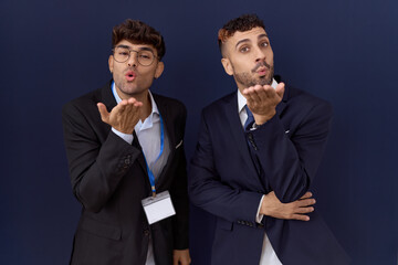 Poster - Two hispanic business men wearing business clothes looking at the camera blowing a kiss with hand on air being lovely and sexy. love expression.