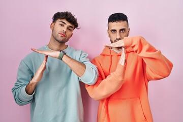 Wall Mural - Young hispanic gay couple standing over pink background doing time out gesture with hands, frustrated and serious face