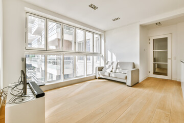 a living room with wood flooring and white walls, including a large window that looks out onto the street