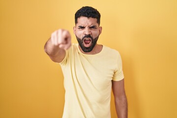 Wall Mural - Hispanic man with beard standing over yellow background pointing displeased and frustrated to the camera, angry and furious with you