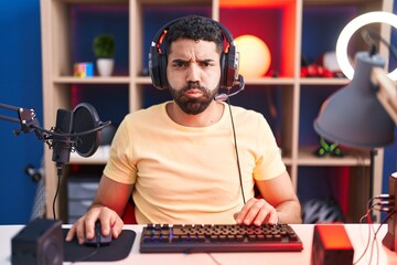 Wall Mural - Hispanic man with beard playing video games with headphones puffing cheeks with funny face. mouth inflated with air, crazy expression.