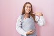 © Krakenimages.com - Young caucasian woman holding and carrying baby on a sling smiling happy pointing with hand and finger