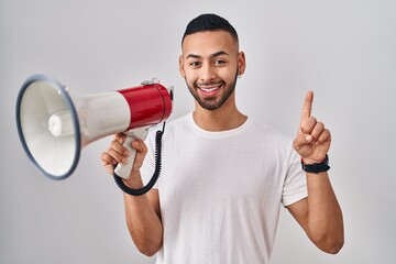 Poster - Young hispanic man shouting through megaphone smiling with an idea or question pointing finger with happy face, number one