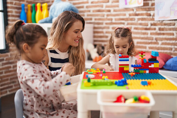 Poster - Teacher with girls playing with construction blocks sitting on table at kindergarten