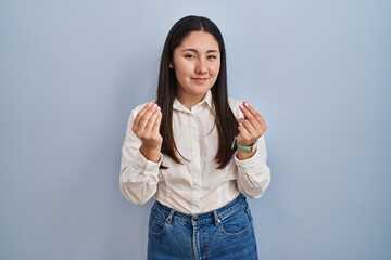 Wall Mural - Young latin woman standing over blue background doing money gesture with hands, asking for salary payment, millionaire business