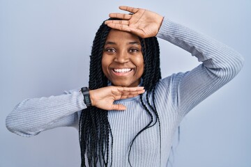 Poster - African american woman standing over blue background smiling cheerful playing peek a boo with hands showing face. surprised and exited