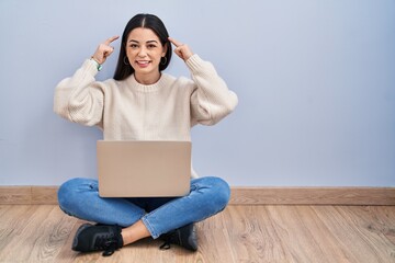 Sticker - Young woman using laptop sitting on the floor at home smiling pointing to head with both hands finger, great idea or thought, good memory