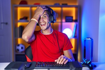 Canvas Print - Young hispanic man playing video games surprised with hand on head for mistake, remember error. forgot, bad memory concept.