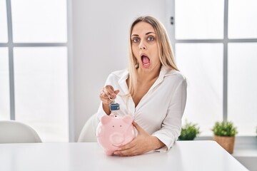 Sticker - Young blonde woman holding piggy bank and house keys afraid and shocked with surprise and amazed expression, fear and excited face.