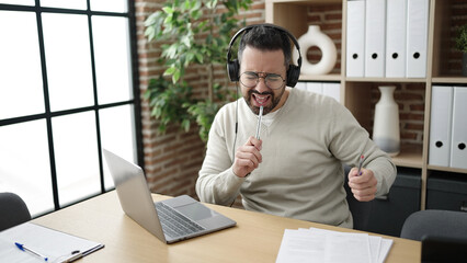 Canvas Print - Young hispanic man business worker listening to music doing drummer gesture at office