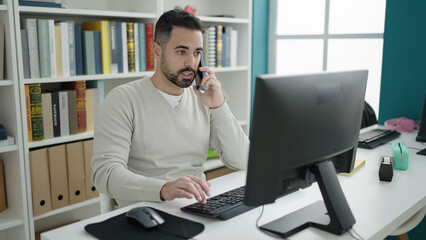 Sticker - Young hispanic man student using computer talking on smartphone at library university