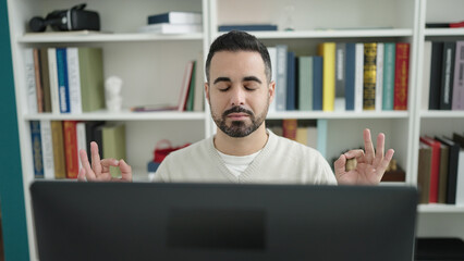 Sticker - Young hispanic man student doing yoga exercise at library university