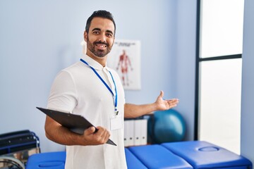 Sticker - Young hispanic man physiotherapist smiling confident holding clipboard at rehab clinic