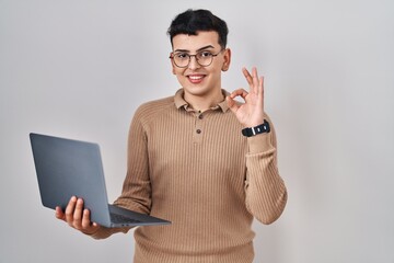 Wall Mural - Non binary person using computer laptop smiling positive doing ok sign with hand and fingers. successful expression.