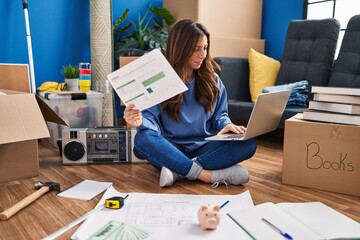 Canvas Print - Young hispanic woman smiling confident using laptop and reading document at new home