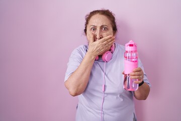 Sticker - Senior woman wearing sportswear and headphones shocked covering mouth with hands for mistake. secret concept.