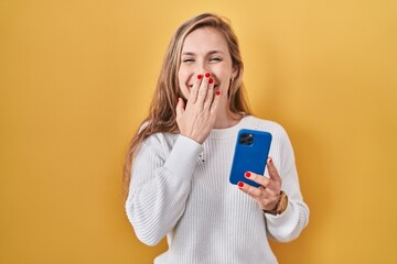 Poster - Young blonde woman using smartphone typing message laughing and embarrassed giggle covering mouth with hands, gossip and scandal concept