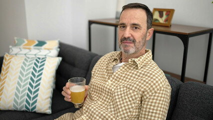 Sticker - Middle age man holding glass of beer sitting on sofa at home