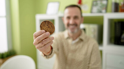 Sticker - Middle age man holding cookie sitting on table at home