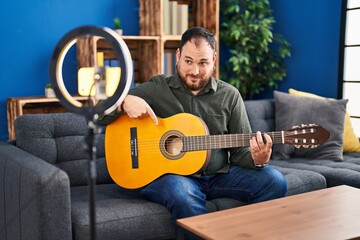 Wall Mural - Plus size hispanic man with beard playing classic guitar at music studio recording himself smiling happy pointing with hand and finger