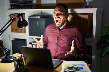 Canvas Print - Plus size hispanic man with beard working at the office at night crazy and mad shouting and yelling with aggressive expression and arms raised. frustration concept.