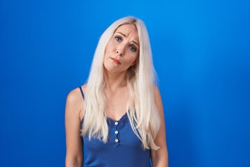 Wall Mural - Caucasian woman standing over blue background looking sleepy and tired, exhausted for fatigue and hangover, lazy eyes in the morning.