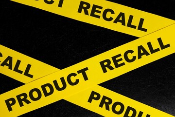 Product recall alert, caution and warning concept. Yellow barricade tape with word in dark black background.