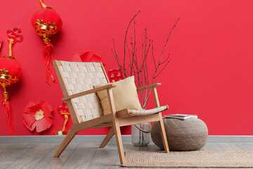 Stylish armchair and pouf near red wall with beautiful Chinese print in room