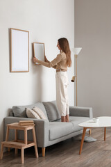 Poster - Young woman hanging blank frame on light wall at home