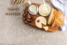 The Feast Of The Giving Of The Torah. Dairy Products, Bread, Grapes. The Concept Of The Jewish Holiday. Grey Background With Letters - Happy Shavuot.