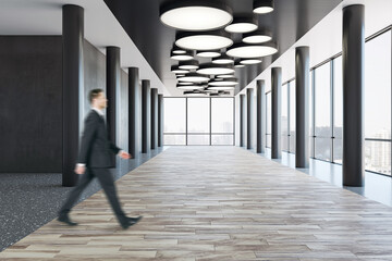 Aufkleber - Side view on blurred walking businessman on wooden floor in spacious empty business center corridor with stylish lamps on dark top, black pillars in front panoramic windows with city view background