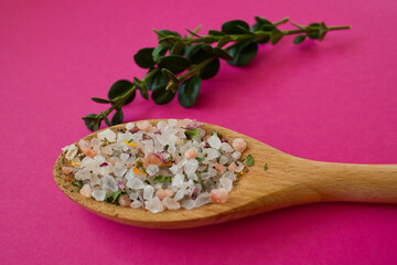 herbal salt on a wooden spoon on a pink background with a green leaf