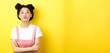 Cute teen asian girl pucker lips for kiss, cross arms on chest and look romantic at camera, yellow background