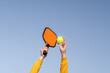 pickleball game, hands over blue sky hitting pickleball yellow ball with paddle, outdoor sport leisure activity