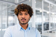 © Liubomir - Close-up portrait of young successful hispanic businessman inside office, man in blue shirt concentrating and thinking looking at camera, programmer at workplace with curly hair.