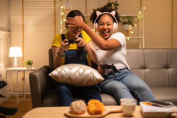 young asian and african woman playing video games at home living room at night.lesbian couples or lg