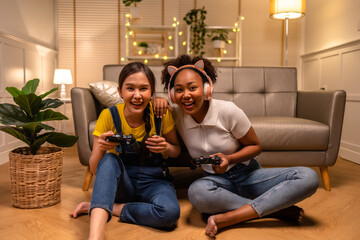 Wall Mural - Young  asian and african woman playing video games at home living room at night.Lesbian couples or lgbt activities on vacation inside the room.