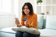 © Prostock-studio - Purchasing Online. Smiling Arab Woman Using Smartphone And Credit Card At Home