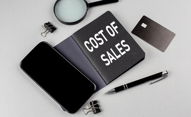 Wall Mural - COST OF SALES text written on black notebook with smartphone, magnifier and credit card