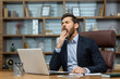 © Liubomir - Mature man yawning inside classic office, senior businessman in workplace sleepless and overworked, boss in business suit sitting at desk, using laptop at work.