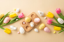 Easter Concept. Top View Photo Of Colorful Easter Eggs In Wooden Holder Ceramic Easter Bunnies Yellow And Pink Tulips On Isolated Pastel Beige Background